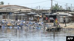 FILE: People pass near a dumping ground for plastic and other waste on the edge of the Ebrie lagoon in Abidjan on July 22, 2022. - Once a prized feature of Abidjan and its surroundings, the "pearl of lagoons" has become a victim of plastic pollution on a vast scale.
