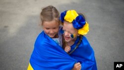 Ukrainian refugee children play wrapped in Ukraine's flag during an event marking the country's Independence Day and the six-month milestone of Russia's invasion, in Bucharest, Romania, Aug. 24, 2022.