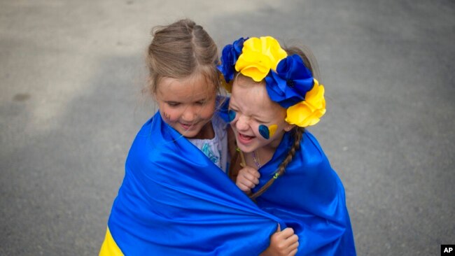 Niños refugiados ucranianos juegan envueltos en la bandera de Ucrania durante un evento que marca el Día de la Independencia del país y el hito de seis meses de la invasión de Rusia, en Bucarest, Rumania, el 24 de agosto de 2022.