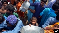 Displaced families line up to receive food as they take refuge on a roadside after fleeing their flood-hit homes in Sohbat Pur city, a district of Pakistan's southwestern Baluchistan province, Aug. 30, 2022.