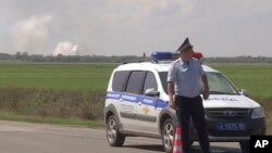 En esta imagen tomada de un video proporcionado por la televisión rusa RU-RTR el 16 de agosto de 2022, un policía bloquea el camino al lugar de la explosión en un depósito de municiones del ejército ruso cerca del pueblo de Mayskoye, Crimea.