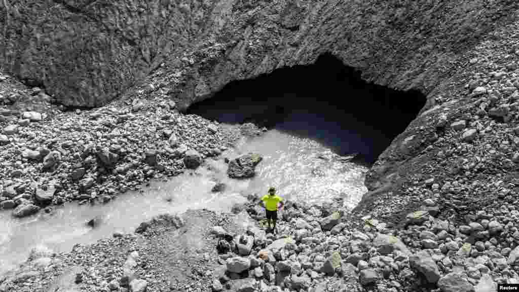 A man stands in front of a hole where water flows out of the Mont Mine glacier in Ferpecle near Evolene, Switzerland, Aug. 29, 2022.