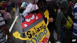 A teacher holds a sign that reads in Spanish: "Living wage now!" during a pro-government protest by public workers demanding the government pay their full benefits and respect collective bargaining agreements in Caracas, Venezuela, Aug. 10, 2022.