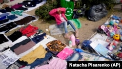 A vendor sits surrounded by her secondhand garments at a market near Buenos Aires, Argentina, Wednesday, Aug. 10, 2022. (AP Photo/Natacha Pisarenko)