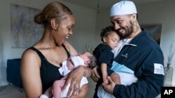 Aaliyah Wright, 25, of Washington, reacts on seeing a smile from her newborn daughter Kali, as her husband Kainan Wright, 24, of Washington, holds their son Khaza, 1, during a visit to the children's grandmother in Accokeek, Maryland, Aug. 9, 2022.