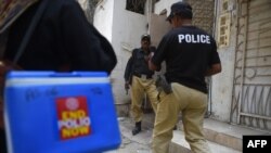 Polisi mengawal anggota tim vaksinasi polio selama kampanye vaksinasi dari pintu ke pintu di Karachi, 28 Juni 2022. (Foto: Rizwan TABASSUM / AFP)