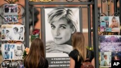 Dua orang perempuan tampak mengamati koleksi foto dari Putri Diana yang dipasang di gerbang Istana Kensington di London, pada 30 Agustus 2022. Kumpulan foto Diana dipajang untuk mengenang 25 tahun kematiannya dalam sebuah kecelakaan di Paris. (Foto: AP/Alastair Grant)