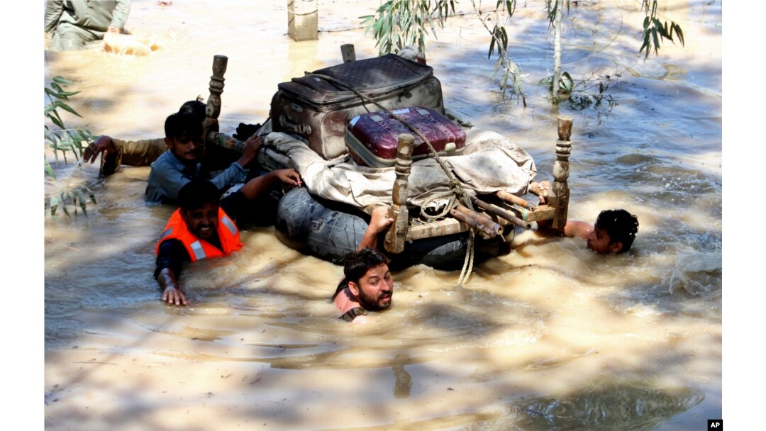 Displaced people float belongings salvaged from flood-hit homes through a flooded area, on the outskirts of Peshawar, Pakistan, Aug. 28, 2022.