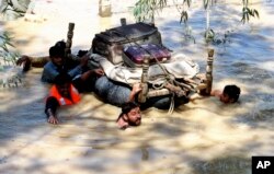 Displaced people float belongings salvaged from flood-hit homes through a flooded area, on the outskirts of Peshawar, Pakistan, Aug. 28, 2022.