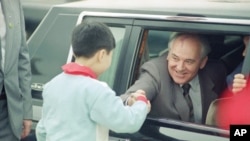 FILE - Soviet General Secretary Mikhail Gorbachev leans out of the window of his limousine to shake the hand of a Chinese child on hand to greet him as he arrived at Shanghai Airport on May 19, 1989, in Shanghai, China.