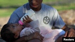 Evangeline, de 1 año, bebe de su botella mientras espera con su padre, Juan Camilo Mendoza, a su madre, Noralis Zuniga, afuera del Mary's Center en Washington, EEUU, el 23 de agosto de 2022.