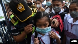 A city hall employee helps a student put on a face mask during the opening of classes at a school in Quezon City, suburban Manila on Aug. 22, 2022, as millions of children in the Philippines returned to school, with many taking their seats in classrooms f