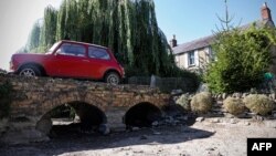 A vintage Mini is parked on the driveway over the dry riverbed of the Infant River Thames in Ashton Keynes, England, on Aug. 8, 2022. The source of the Thames has dried up and has shifted more than five miles downstream. Villagers say they last saw the river dry in 1976.