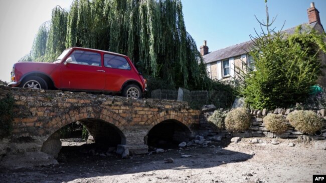 A vintage Mini is parked on the driveway over the dry riverbed of the Infant River Thames in Ashton Keynes, England, on Aug. 8, 2022. The source of the Thames has dried up and has shifted more than five miles downstream. Villagers say they last saw the river dry in 1976.