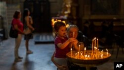 A child is held by his grandmother as they light a candle in a church in Lviv, Ukraine, Aug. 26, 2022.