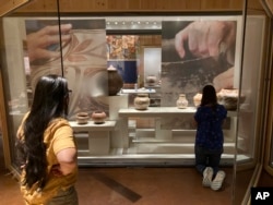 Elysia Poon, director of the Indian Arts Research Center in New Mexico, at left, oversees finishing touches on a community-curated exhibition of Native American pottery from the Pueblo Indian region of the U.S. Southwest on July 28, 2022, at the Museum of Indian Arts and Culture in Santa Fe, N.M. (AP Photo/Morgan Lee)
