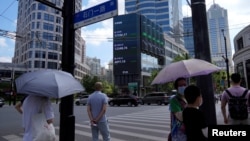 Pedestrians wait to cross a road at a junction near a giant display of stock indexes in Shanghai, Aug. 3, 2022. China's financial hub said, Aug. 14, 2022, it would reopen all schools on Sept. 1 after months of COVID-19 closures.