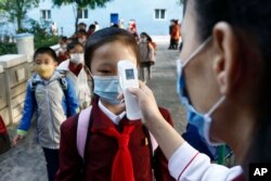 Seorang guru mengukur suhu tubuh seorang siswi sebelum memasuki Sekolah Dasar Kim Song Ju di Distrik Pusat di Pyongyang, Korea Utara, pada 13 Oktober 2021. (Foto: AP)