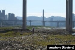 一名女子走过因干旱而裸露在外的重庆段长江河床。（2022年8月17日）