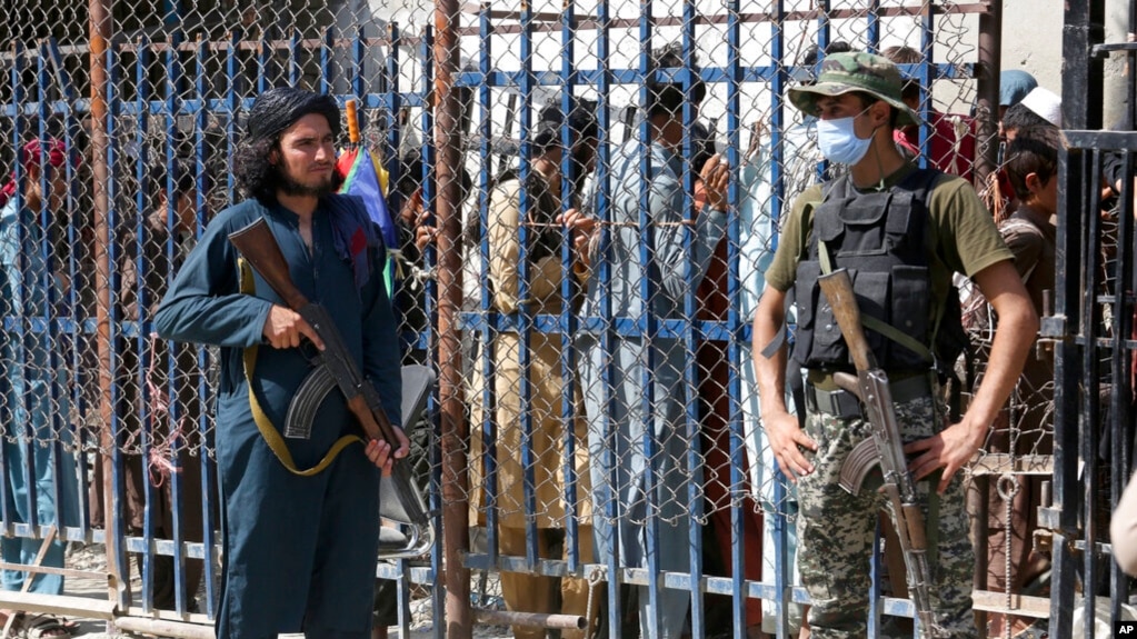 یک سرباز شبه‌نظامی پاکستانی، راست، و یک جنگجوی طالبان در گذرگاه مرزی پاکستان و افغانستان - ۲۱ اوت ۲۰۲۱