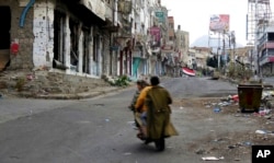 FILE - Men ride through streets wrecked by fighting in Taiz, Yemen, Feb. 4, 2018.