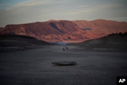 FILE - A formerly sunken boat sits on cracked earth hundreds of feet from what is now the shoreline on Lake Mead on May 9, 2022, near Boulder City, Nevada. Two sets of human remains emerged from the drought-stricken Colorado River reservoir just a short drive from Las Vegas, Nevada. (AP Photo/John Locher)