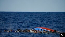 Migrants swim next to their overturned wooden boat during a rescue operation by Spanish NGO Open Arms south of the Italian island of Lampedusa in the Mediterranean Sea.