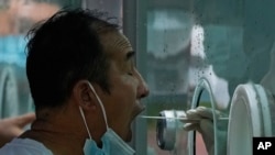 A man pulls his mask to get his routine COVID-19 throat swab at a coronavirus testing site in Beijing, Aug. 9, 2022. 