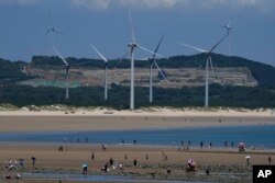 FILE - Beachgoers walk near wind turbines along the coast of Pingtan in Southern China's Fujian province, Aug. 6, 2022.