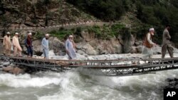 Des personnes traversent une rivière sur un pont endommagé par les eaux de crue, dans la ville de Bahrain, au Pakistan, le 30 août 2022.