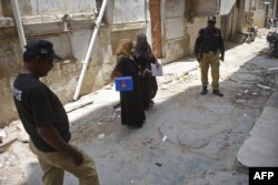 Polisi mengawal anggota tim vaksinasi polio selama kampanye vaksinasi dari pintu ke pintu di Karachi, 28 Juni 2022. (Rizwan TABASSUM / AFP)