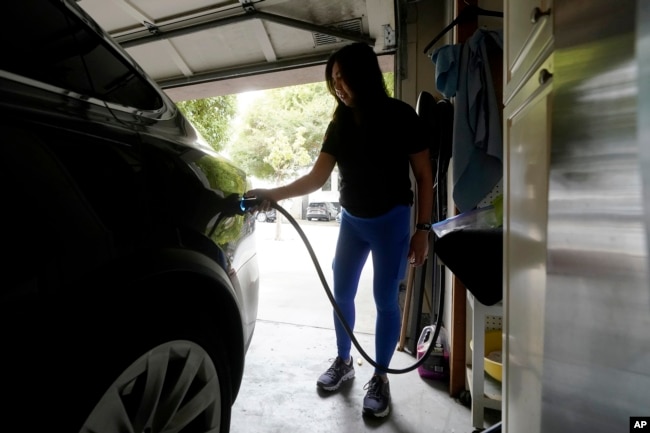 Monique An charges her Tesla car to a wall connector charger while posing for photos at her home in San Francisco, Thursday, Aug. 25, 2022. (AP Photo/Jeff Chiu)