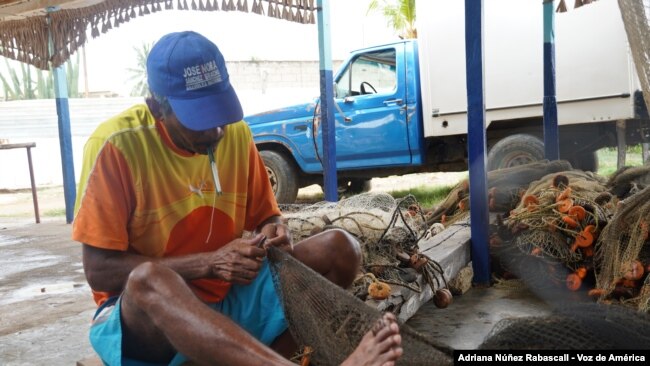 Un pescador intenta sacar las manchas de petróleo de su red