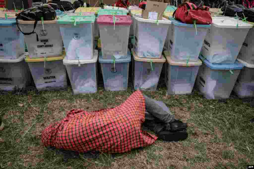 An election presiding officer sleeps next to ballot boxes as he waits to return all electoral materials following Kenya&#39;s general election at the tallying center in Kilgoris.