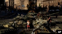 Varias personas caminan entre vehículos militares rusos destruidos instalados en el centro de Kiev, Ucrania, el 24 de agosto de 2022. 