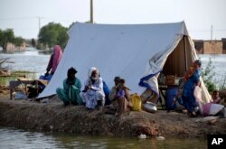 A family sits near their tent surrounded by water, in Sohbat Pur city of Jaffarabad, a district of Pakistan's southwestern Baluchistan province, Sunday, Aug. 28, 2022.