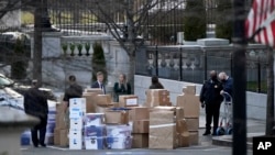 ARCHIVO - La gente espera un camión de mudanzas después de que sacaron cajas del edificio de la Oficina Ejecutiva Eisenhower dentro del complejo de la Casa Blanca, el 14 de enero de 2021, en Washington.