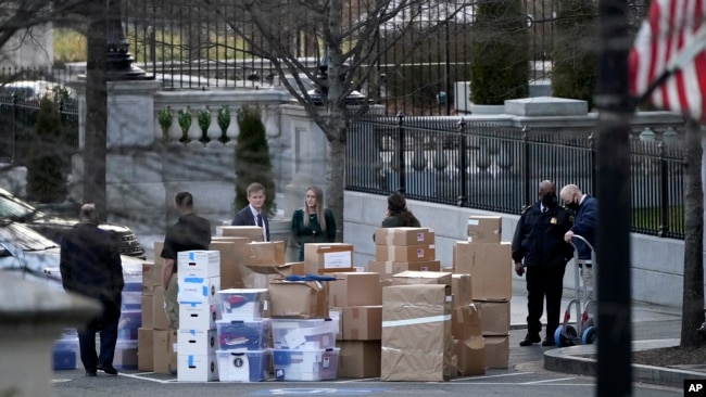 ARCHIVO - La gente espera un camión de mudanzas después de que sacaron cajas del edificio de la Oficina Ejecutiva Eisenhower dentro del complejo de la Casa Blanca, el 14 de enero de 2021, en Washington.