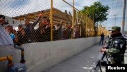 Migrants stand by the fence of a temporary shelter for migrants in Piedras Negras, Mexico, Feb. 7, 2019. 