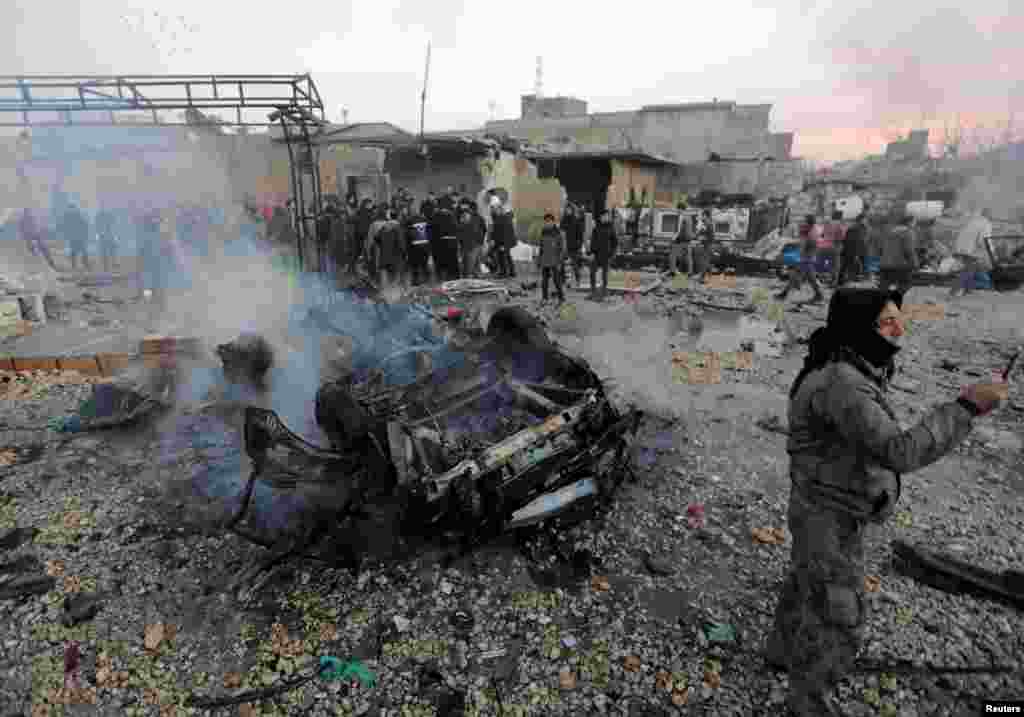 A man takes a picture near a burnt car at the site of a truck blast in Azaz, Syria.