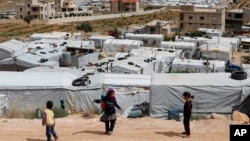 FILE - Syrian refugee children play at an informal refugee camp, which is seen set between the houses and buildings in Arsal, near the border with Syria, east Lebanon, June 13, 2018.
