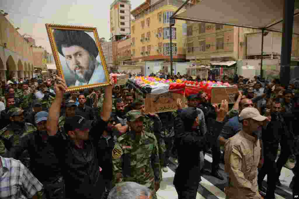 Mourners chant slogans against the Islamic State group as they carry the flag-draped coffins of three members of the Peace Brigades, a Shi&#39;ite militia group loyal to Shi&#39;ite cleric Muqtada al-Sadr, who were killed during fighting with Islamic State militants, during the funeral in Najaf, south of Baghdad, May 27, 2015. 