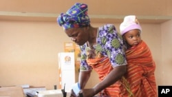 A woman with a child on her back casts her vote at a polling station as the country goes to the polls in Maputo, Mozambique, Oct. 15, 2014.