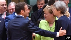 French President Emmanuel Macron (left) puts his hand on the shoulder of British Prime Minister Theresa May during a round table meeting at an EU summit in Brussels, June 22, 2017. German Chancellor Angela Merkel stands between them.