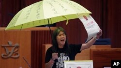 Newly elected pro-democracy lawmaker Leung Kwok-hung, known as "Long Hair," holds a yellow umbrella and a oversized mock copy of controversial, proposed anti-subversion legislation as she takes oath in the new legislature Council in Hong Kong, Oct. 12, 20