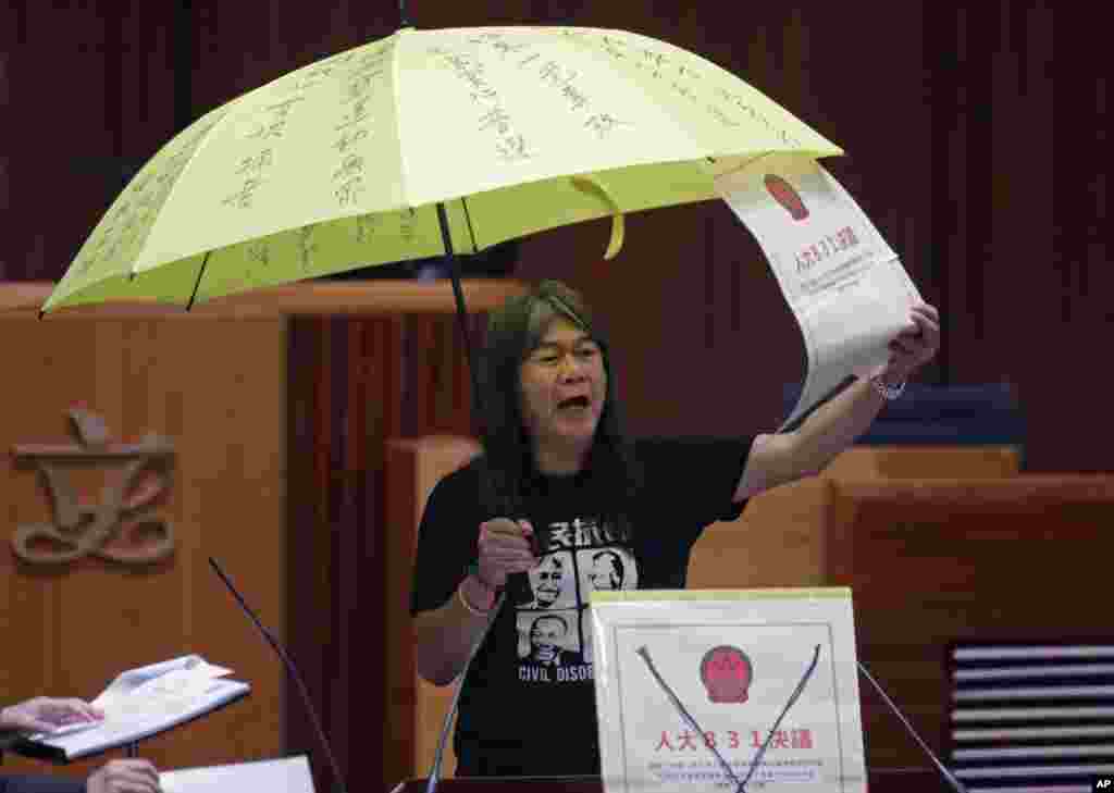 Newly elected pro-democracy lawmaker Leung Kwok-hung, known as "Long Hair," holds a yellow umbrella and an oversized mock copy of controversial, proposed anti-subversion legislation as she takes her oath in the new legislature Council in Hong Kong.