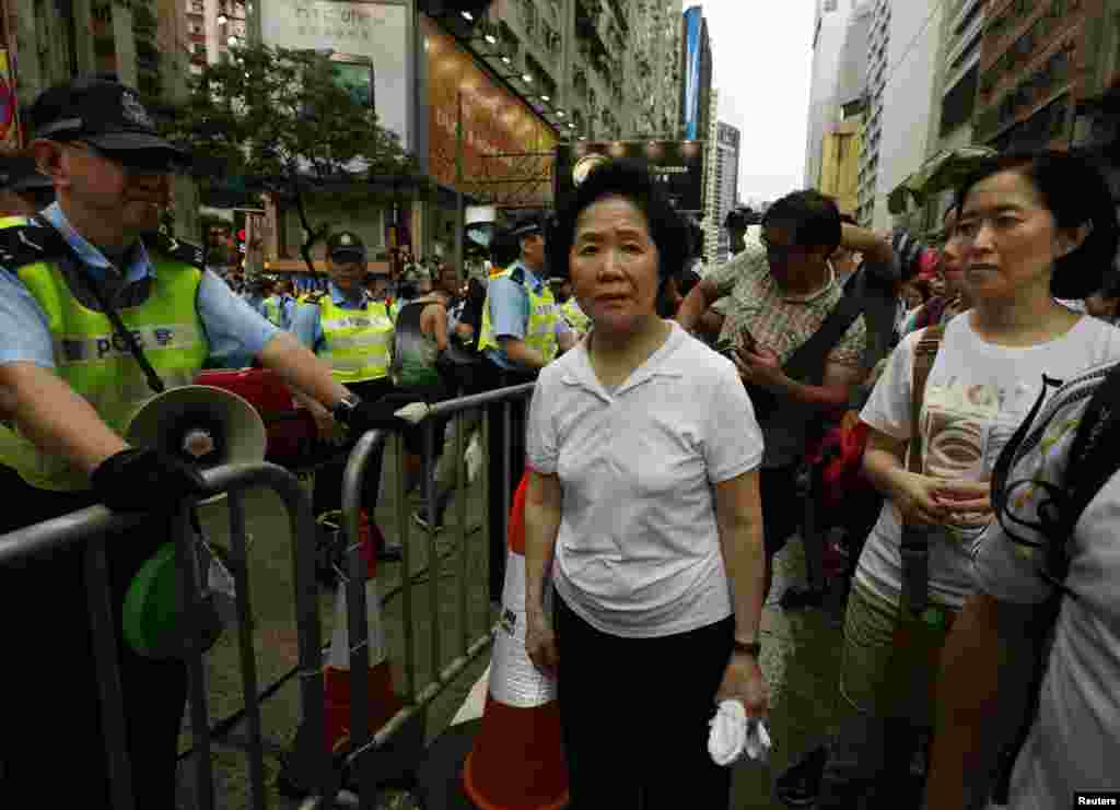Former Hong Kong Chief Secretary Anson Chan (center) looks on beside a police officer as she joins thousands of protesters during a march to demand universal suffrage in Hong Kong, July 1, 2014.