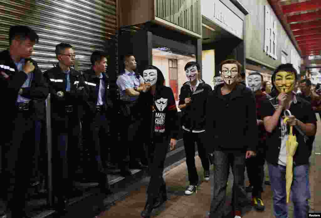 Pro-democracy protesters wearing Guy Fawkes masks walk past policemen on a road occupied by protesters as part of the Occupy Central civil disobedience movement at Mongkok district, Hong Kong, Nov. 5, 2014.