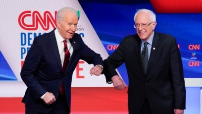 Mantan wakil presiden AS Joe Biden (kiri) dan Senator Bernie Sanders (kanan) saling menyapa sebelum debat Pilpres 2020 di Studio CNN di Washington, Minggu, 15 Maret 2020. (Foto: AP)