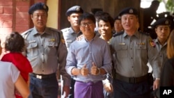 Reuters journalist Wa Lone, center, flashes thumps up as he is escorted by Myanmar police to court for trial, Feb. 1, 2018, on the outskirts of Yangon, Myanmar. The trial resumes for the two Reuters journalists charged of violating state secrets.